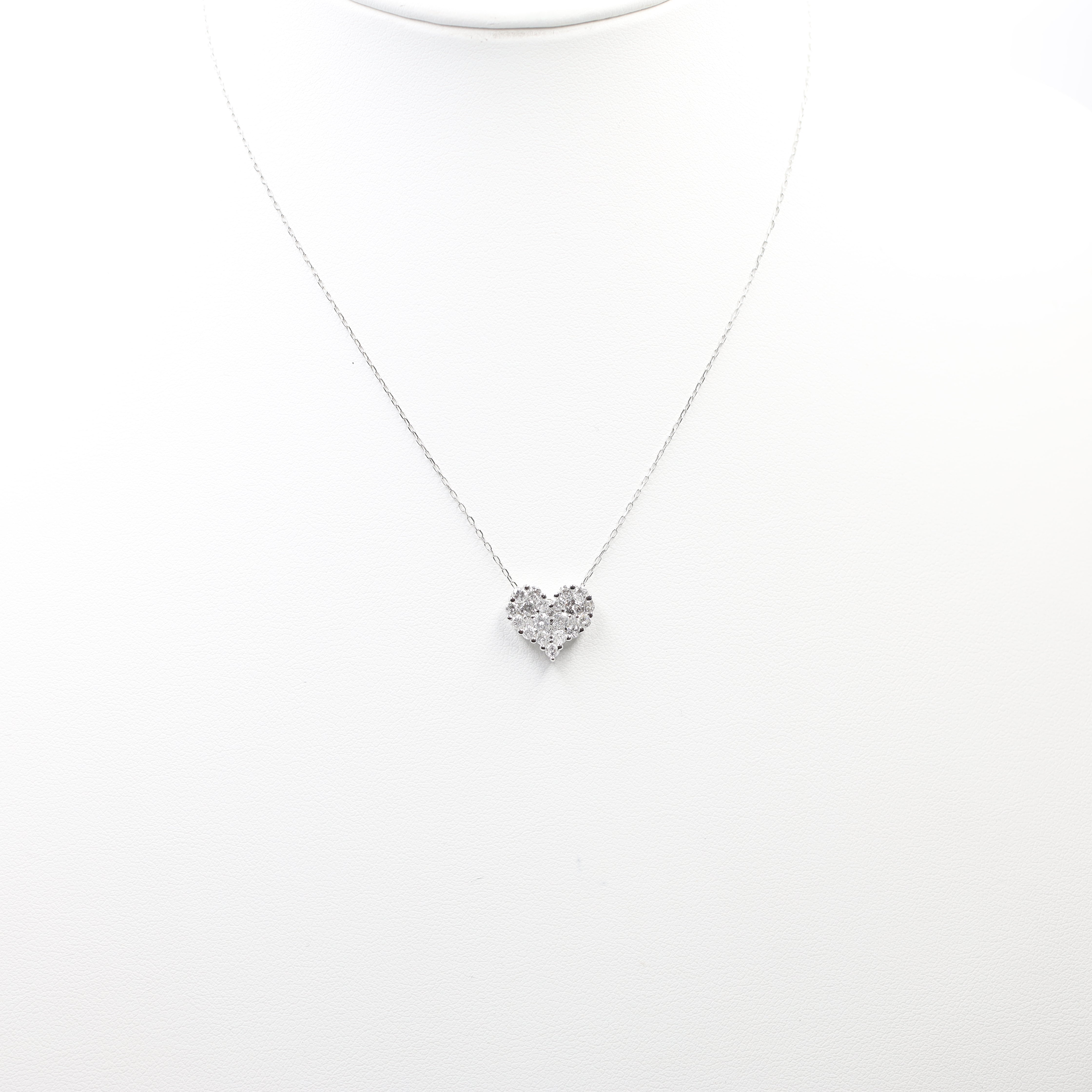 A dazzling heart-shaped diamond pendant necklace, set on a delicate white metal chain. The heart is formed by a cluster of sparkling diamonds, creating a romantic and brilliant look.